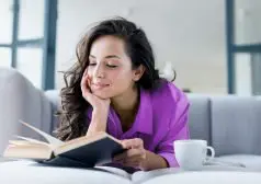 אשה קוראת ספר לצד ספל קפה